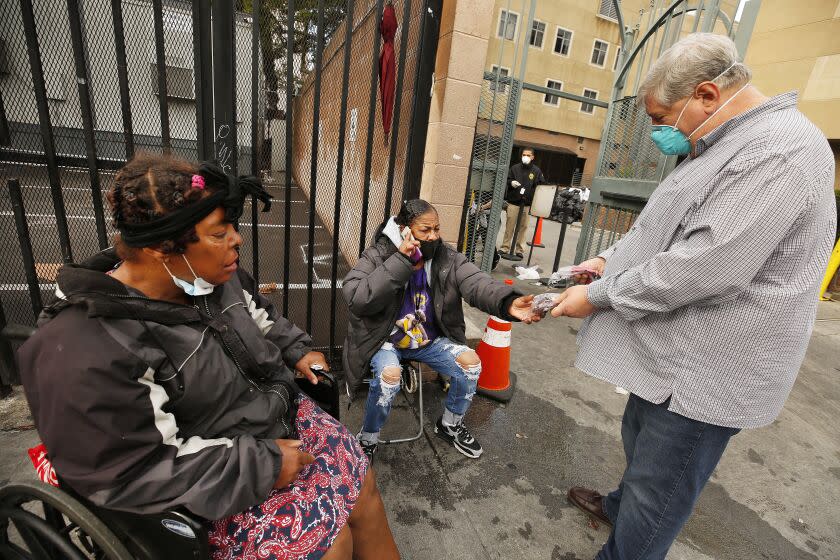 Herb Smith, right, President/CEO of the Los Angeles Mission in Skid Row area of downtown Los Angeles gives face masks to Carmen Santiago and Juanita Glover, left, as they form a line to receive bags of food and hygiene products distributed to homeless people on Wednesday mornings. The staff is working to maintain safety with masks and social distancing as they serve those in need. Skid Row on Wednesday, April 8, 2020 in Los Angeles, CA.