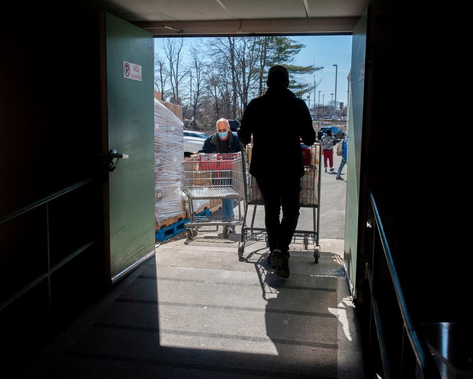 Stephen Nicholson, left, a Sudbury resident who volunteers at the Pearl Street Cupboard & Cafe at Park in Framingham, brings in an empty cart as a client wheels out groceries, March 22, 2024. Paul Mina, president and CEO of the  United Way of Tri-County, reports that in just the past 18 months, demand for food has increased by 85%.