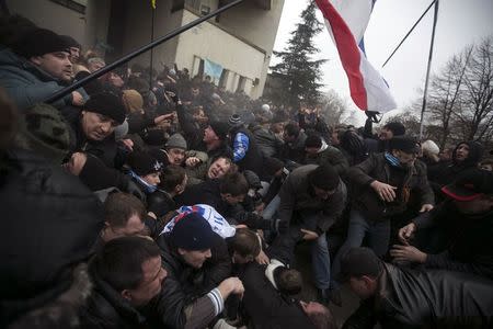 Ukrainian men help pull one another out of a stampede as a flag of Crimea is seen during clashes at rallies held by ethnic Russians and Crimean Tatars near the Crimean parliament building in Simferopol in this February 26, 2014 file photo. REUTERS/Baz Ratner/Files