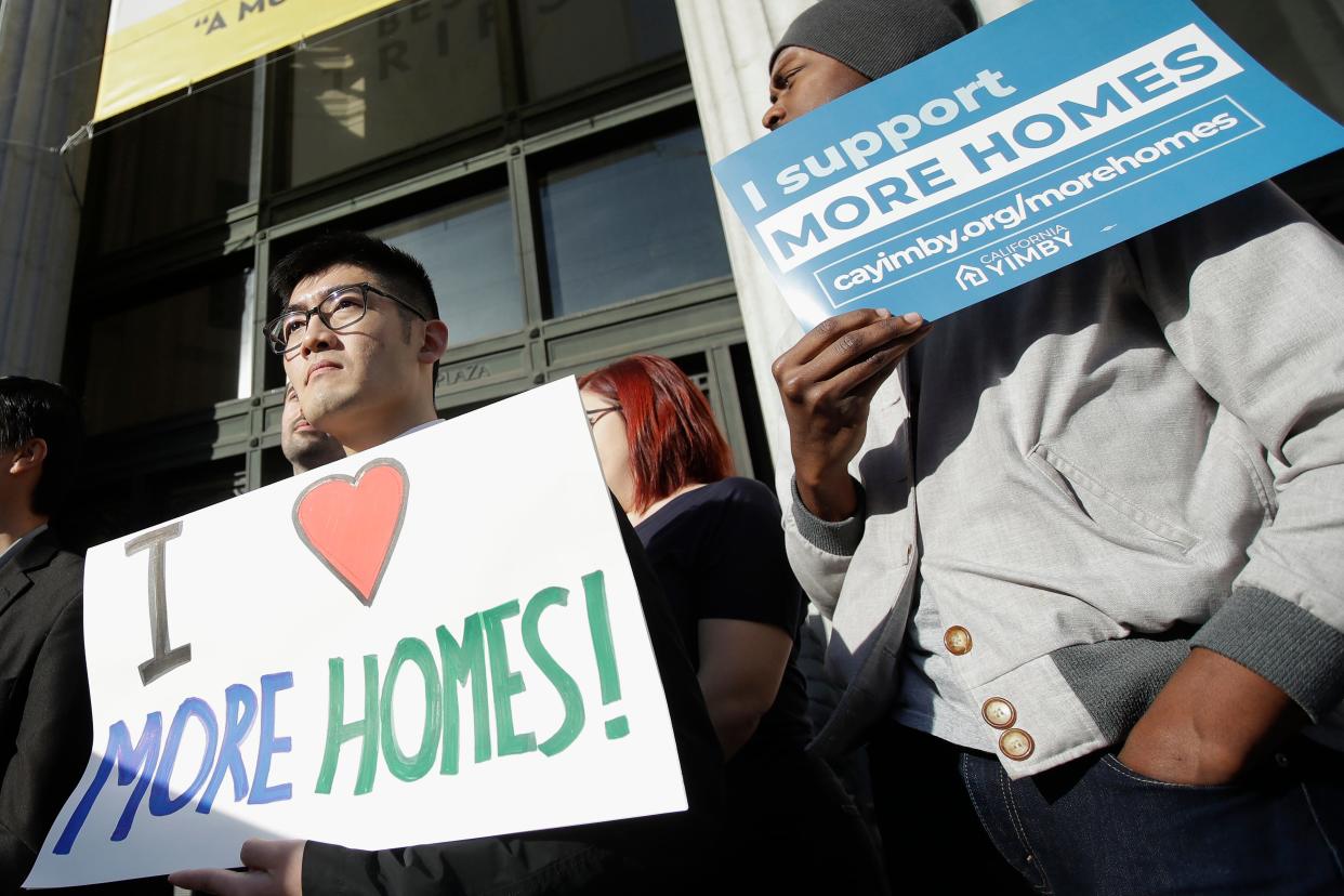 In this Tuesday photo, men hold up signs at a rally on the housing crisis outside City Hall in Oakland. California's Gov. Gavin Newsom said he is seeking $750 million to help pay rent for people facing homelessness, among other purposes, in the most populous state's latest attempt to fight what he called a national crisis.