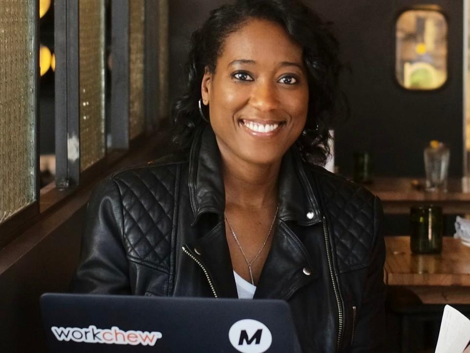 A woman wearing a black jacket in front of a computer smiles to the camera