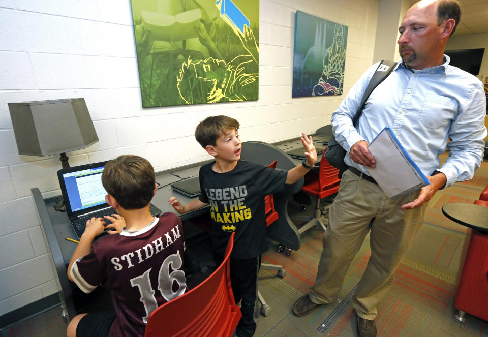 In this May 8, 2019, photograph, Graham Stidham, center, asks his father, East Webster High School Assistant Principal Corey Stidham, for a few more minutes of internet use so his brother, Miles, left, can finish his educational game, at the school's laptop bank in Maben, Miss. The Stidhams are unable to get internet at their rural home, so they take advantage of the internet in the school's library to do homework. (AP Photo/Rogelio V. Solis)