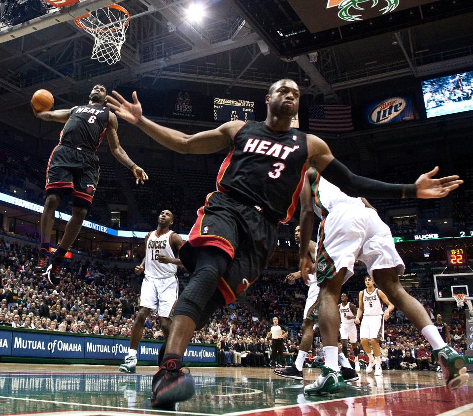 Miami Heat's Dwyane Wade reacts as teammate LeBron James goes up for a dunk during the first half of a game against the Milwaukee Bucks.