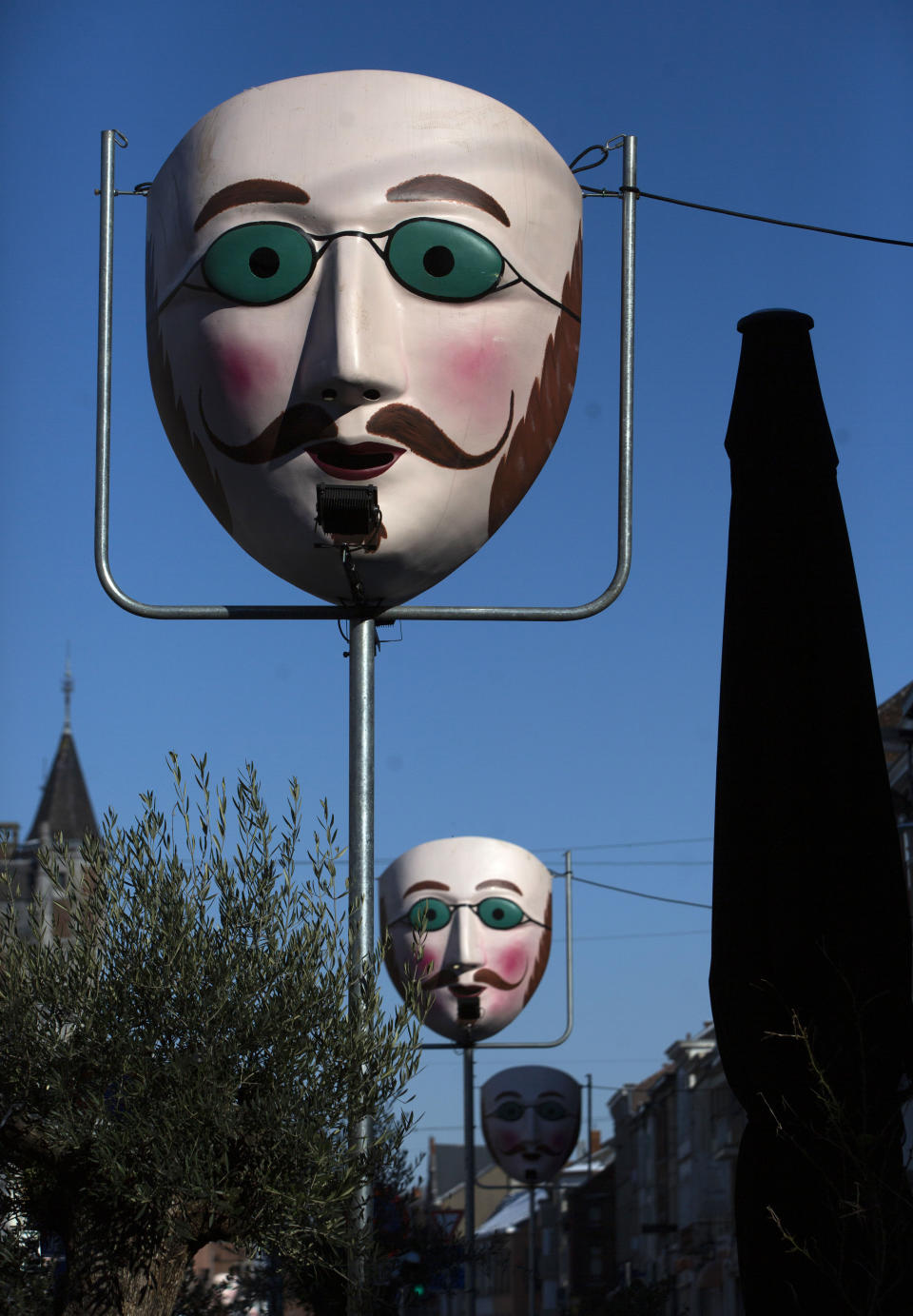 Giant re-creations of the cotton and wax mask worn by the Gilles de Binche sit atop of poles in Binche, Belgium, Thursday, Feb. 11, 2021. In normal life, the small town of Binche in southern Belgium would be bursting with excitement for the carnival festivities that have been labeled a 'Masterpiece of the Oral and Intangible Heritage of Humanity' by UNESCO, but in 2021 the COVID-19 regulations have forced the carnival to be cancelled.(AP Photo/Virginia Mayo)