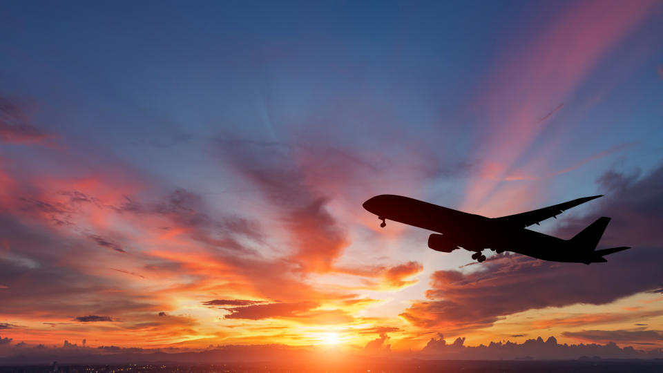 Silhouette of an airplane with sun setting and clouds in the background