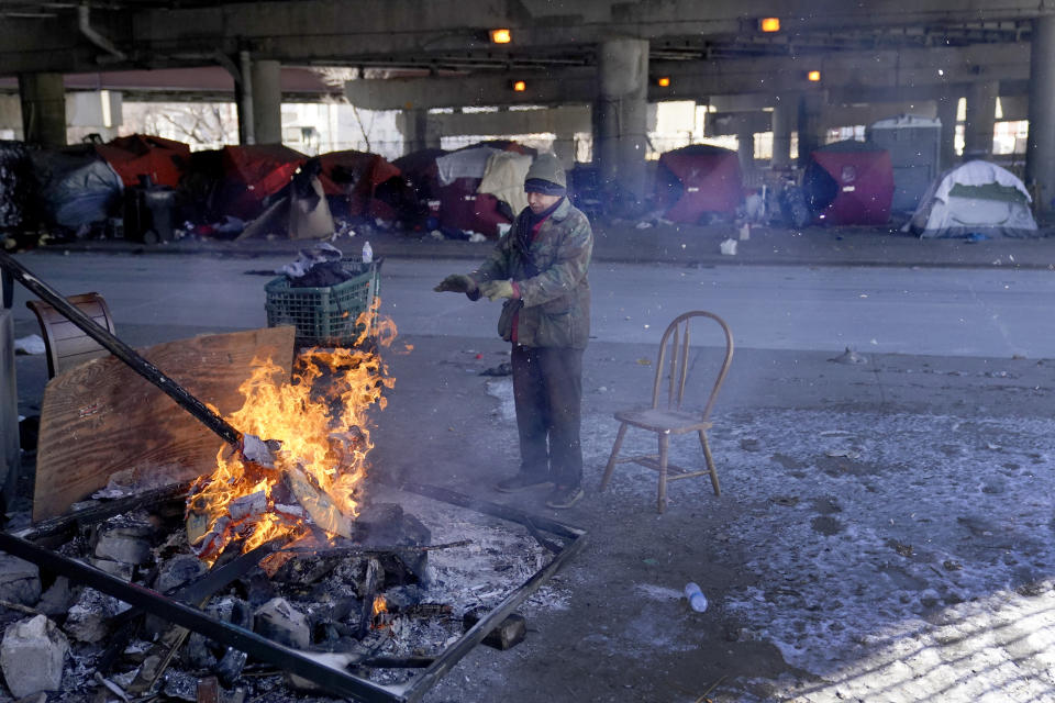 An elderly man warms his hands by the fire he created across the street from a homeless encampment under a major interstate freeway Tuesday, Jan. 16, 2024, in Chicago. (AP Photo/Charles Rex Arbogast)