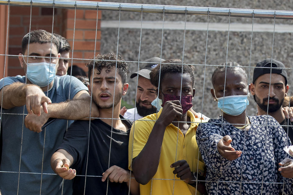 Migrants wait to buy some things standing behind the fence at the refugee camp in the village of Verebiejai, some 145km (99,1 miles) south from Vilnius, Lithuania, Sunday, July 11, 2021. Migrants at the school in the village of Verebiejai, about 140 kilometers (87 miles) from Vilnius, haven't been allowed to leave the premises and are under close police surveillance. Some have tested positive for COVID-19 and have been isolated in the building. (AP Photo/Mindaugas Kulbis)