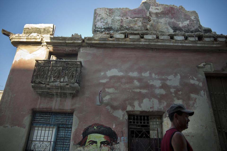 In this April 12, 2014 photo, a man walks past a building that collapsed due to the heavy rain next to an image of revolutionary leader Che Guevara in Havana, Cuba. Despite reforms in recent years to address the island’s housing problem, such building collapses remain common in Cuba, where decades of neglect and a dearth of new apartments has left untold thousands of islanders living in crowded structures at risk of suddenly falling down. (AP Photo/Ramon Espinosa)