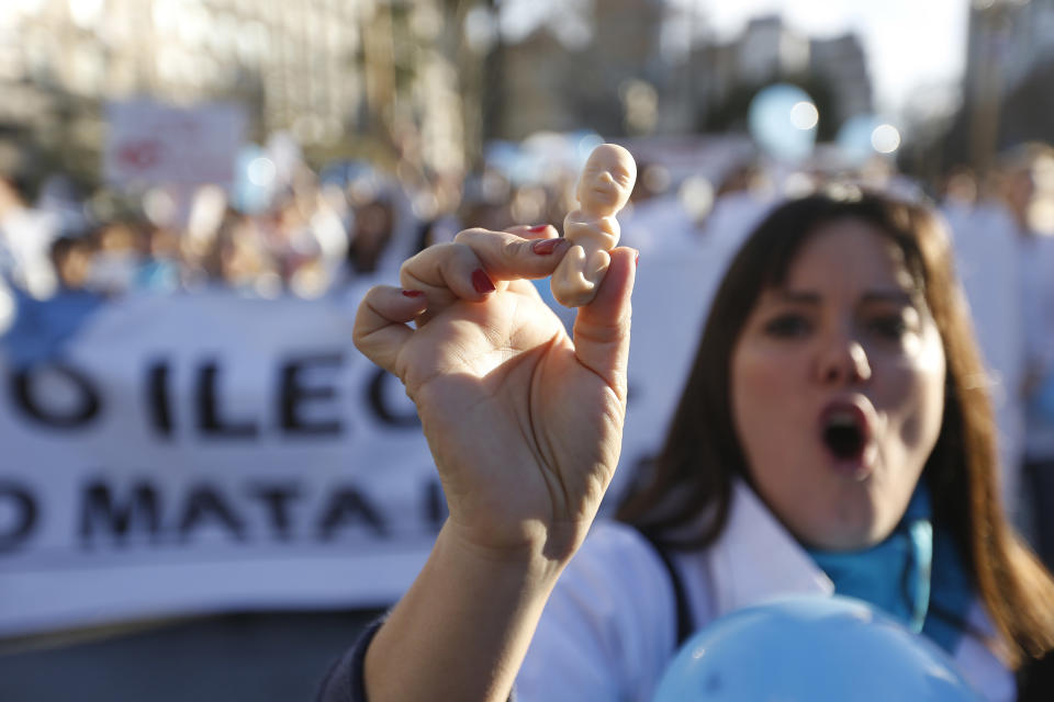 In this July 15, 2018 photo, a medical doctor holds a small plastic doll shaped like a fetus while chanting: "I'm a doctor, not a murderer," during a protest against efforts to legalize abortion, in Buenos Aires, Argentina. A campaign to expand legal abortions is bitterly dividing Argentines and increasingly even the profession that would be asked to carry them out. (AP Photo/Jorge Saenz)