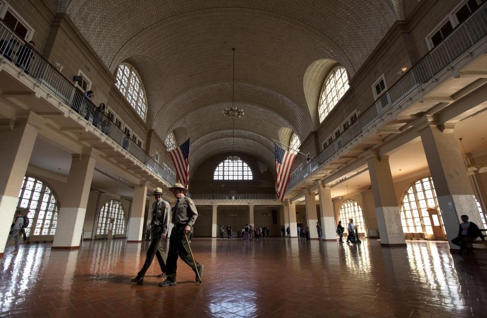FILE - National Park Service rangers walk through the Great Hall at Ellis Island, on April 29, 2015, in New York. The location is featured in a collection of mini-essays by American writers published online by the Frommer's guidebook company about places they believe helped shape and define America. (AP Photo/Julie Jacobson, File)