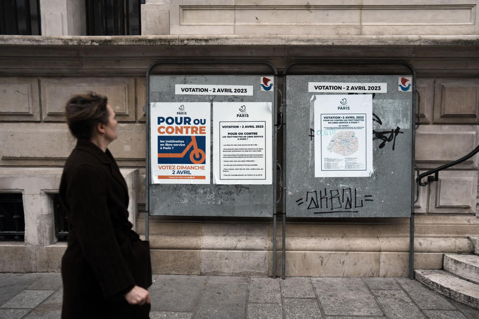 A woman walks by a poster reading "For or against self service scooters in Paris" on the facade of the city hall of the 10th district of Paris, Sunday, April 2, 2023. The wheels may be about to come off Paris' experiment with for-hire electric scooters. That's if Parisians vote on Sunday to do away with the 15,000 opinion-dividing micro-vehicles. (AP Photo/Thibault Camus)