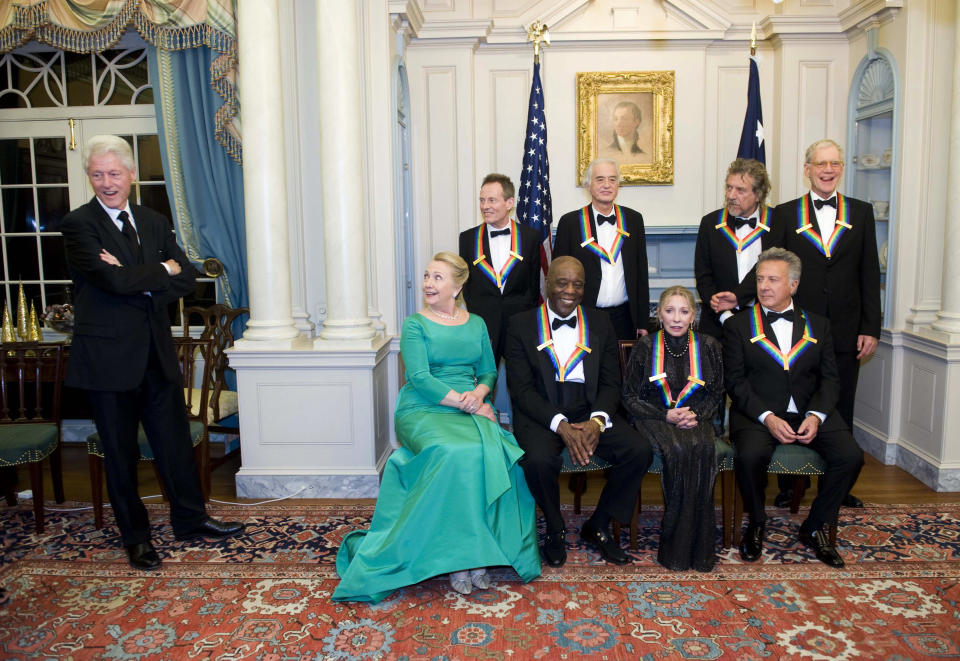 The 2012 Kennedy Center Honorees and Secretary of State Hillary Rodham Clinton, second from left, wait for former President Bill Clinton, left, to join them for a group photo after the State Department Dinner for the Kennedy Center Honors gala Saturday, Dec. 1, 2012 at the State Department in Washington. The 2012 Kennedy Center Honorees are, from left, John Paul Jones, Buddy Guy, Jimmy Page, Natalia Makarova, Robert Plant, Dustin Hoffman, and David Letterman. (AP Photo/Kevin Wolf)