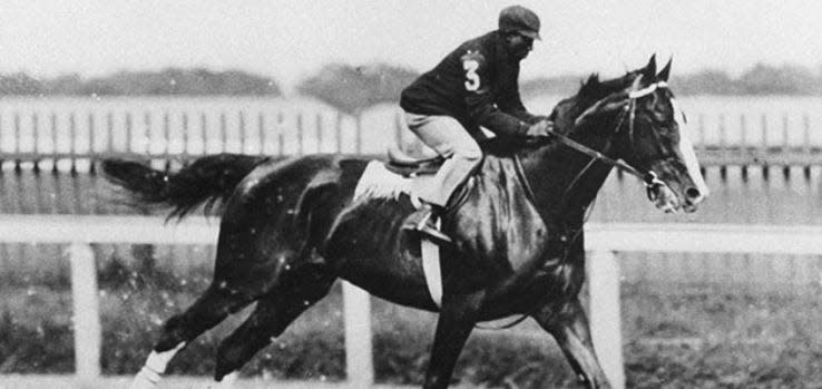 Black jockey James Winkfield racing on a horse.