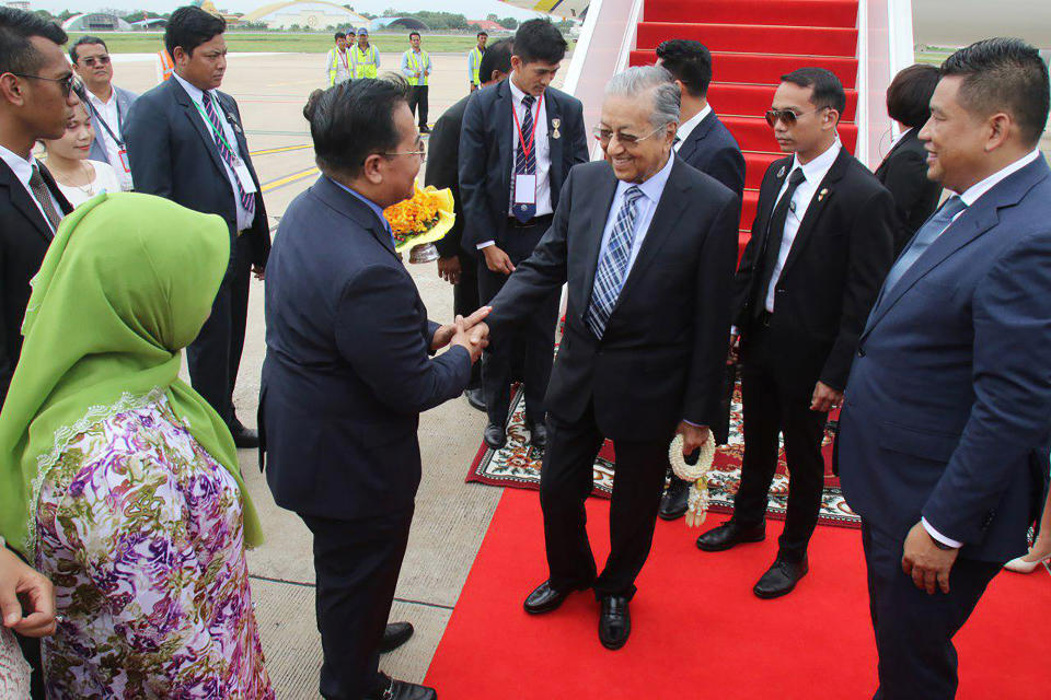 In this photo provided by Agence Kampuchea Presse (AKP), Malaysian Prime Minister Mahathir Mohamad, center, is welcoming by Cambodian government officers upon his arrival at Phnom Penh International Airport, in Phnom Penh, Cambodia. Mahathir Mohamad of Malaysia has arrived in Cambodia for a three-day official visit to strengthen the two countries' bilateral relationship. (Khem Sovannara, Agence Kampuchea Presse via AP)