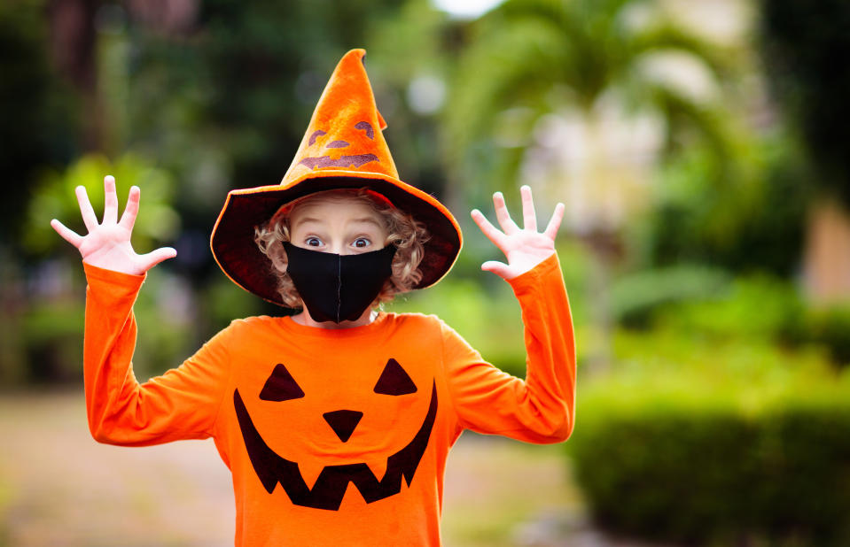 Kids trick or treat in Halloween costume and face mask. Children in dress up with candy bucket in coronavirus pandemic. Little boy and girl trick or treating with pumpkin lantern. Autumn holiday fun.