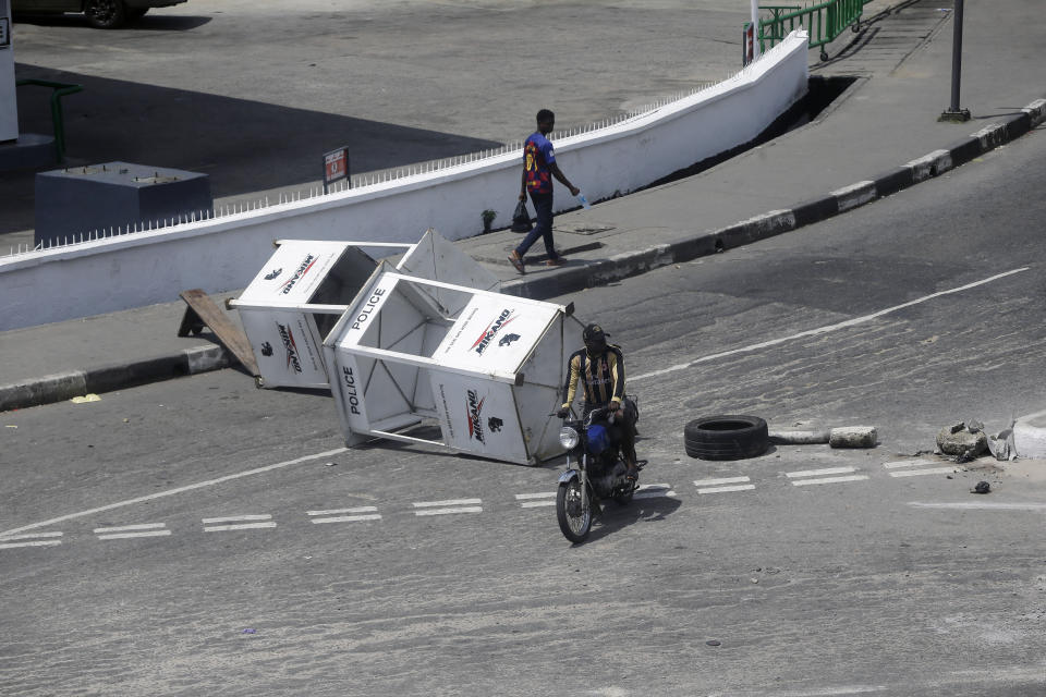 A man rides a Motorcycle taxi past a barricade on a street in Lagos, Nigeria, Thursday Oct. 22, 2020. Lagos streets were empty and shops were shuttered Thursday, as residents of Nigeria's largest city obeyed the government's curfew, stopping the protests against police brutality that had lasted for two weeks. ( AP Photo/Sunday Alamba)