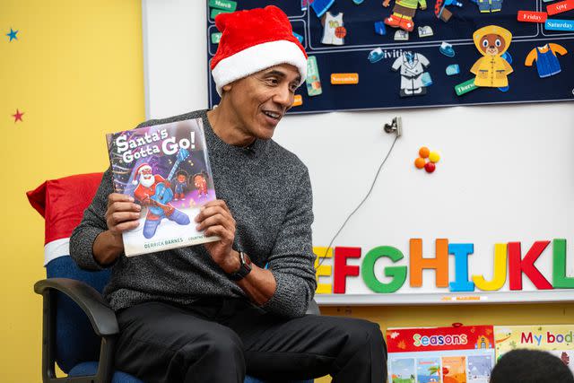 <p>The Obama Foundation</p> President Barack Obama holds up a copy of "Santa's Gotta Go!" by Derrick Barnes