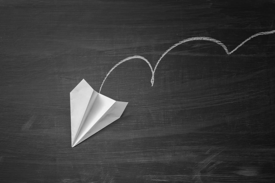 Image of a paper plane in freefall against a black backdrop.