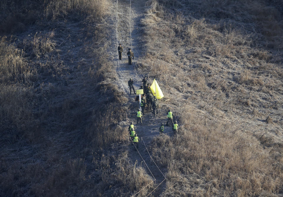 South Korean army soldiers, wearing yellow head bands, cross the Military Demarcation Line inside the Demilitarized Zone (DMZ) to inspect the dismantled North Korean guard post in the central section of the inter-Korean border in Cheorwon, Wednesday, Dec. 12, 2018. South Korea and North Korea have removed some of their guard posts along the border as part of their military agreement last September. (AP Photo/Ahn Young-joon, Pool)