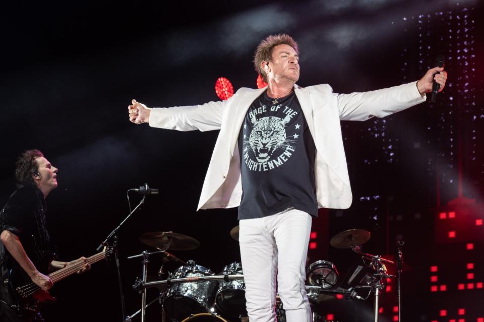 Simon Le Bon standing onstage with arms outstretched.