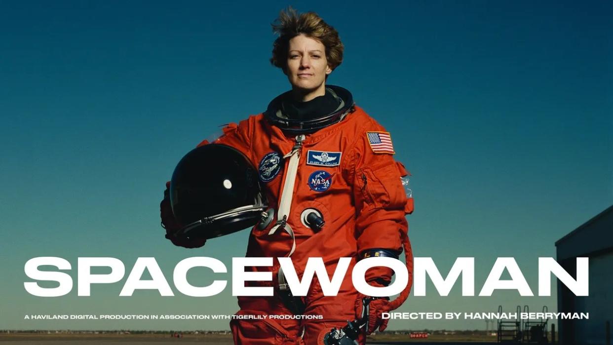  Eileen collins standing in front of a blue sky in an astronaut flight suit, holding a helmet. 