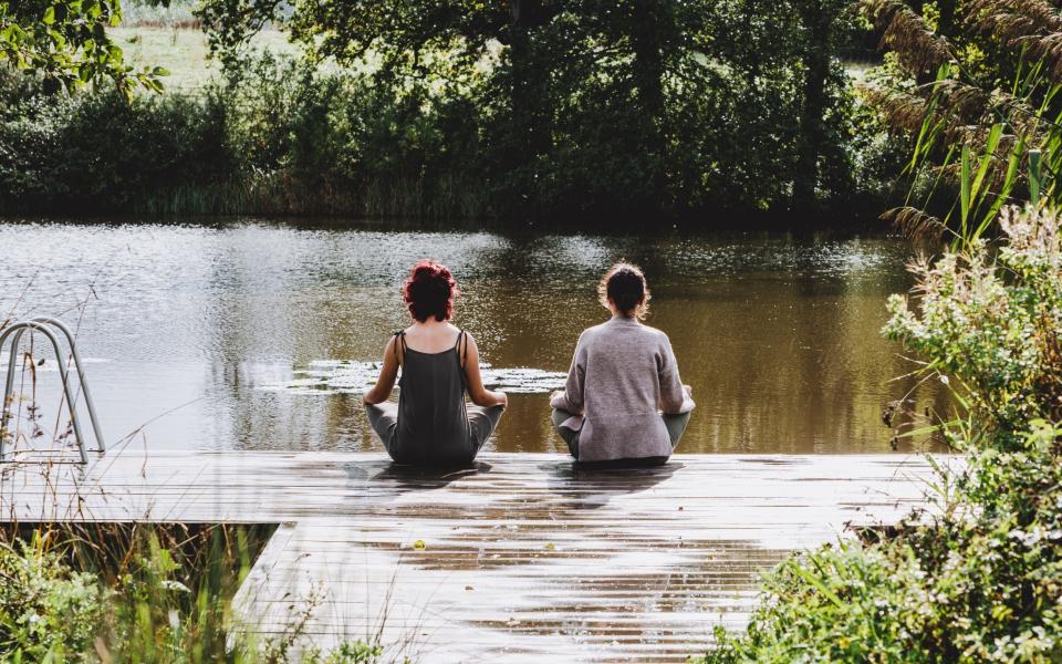 Two women sat meditating by a lake