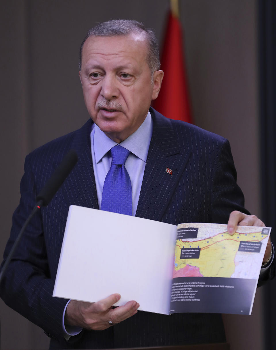 Turkish President Recep Tayyip Erdogan shows a document with a map of Turkey-Syria border as he speaks to reporters before a visit to the United States, in Ankara, Turkey, Tuesday, Nov. 12, 2019. Erdogan warned European nations Tuesday that his country could release all the Islamic State group prisoners it holds and send them to Europe, in response to EU sanctions over Cyprus.(Presidential Press Service via AP, Pool)