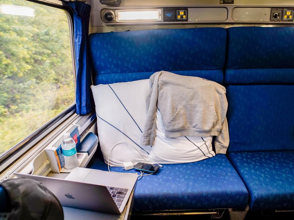 Inside an Amtrak bedroom with blue seats and a big window on the left showing nature outside