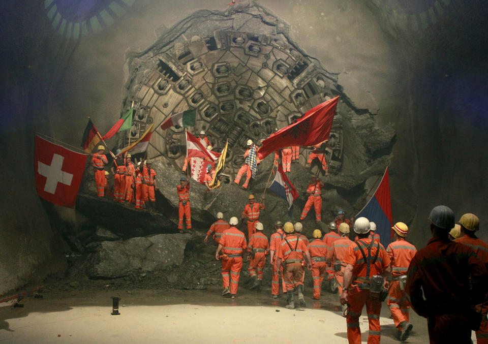 Miners wave with the flags of their home countries as they celebrate as fireworks explode after a giant drill machine broke through the rock at the final section Sedrun-Faido, at the construction site of the NEAT Gotthard Base Tunnel