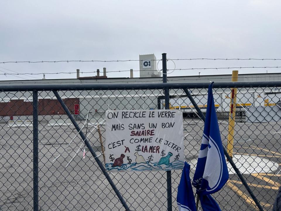 A poster with a slogan that, translated, says 'we recycle glass, but without a good salary, it might as well be thrown in the sea,' hangs in front of the O-I glass factory in Pointe-Saint-Charles, Que. 