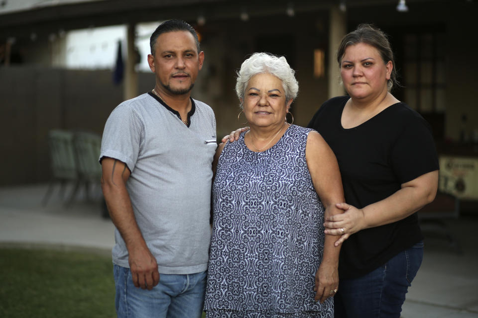 In this July 16, 2020, photo, Rosa Sandoval, center, stands with her son Carlos, left, and daughter Azalia at her home in Phoenix. Rosa said her husband held her face in his hands each time he entered the hospital and said the same thing: "You are so pretty, I love you so much!" The last time Rosa Sandoval heard those words was in mid-June when her husband, Carlos Manuel Sandoval, died after nearly two weeks later from COVID-19 related complications. (AP Photo/Dario Lopez-Mills)