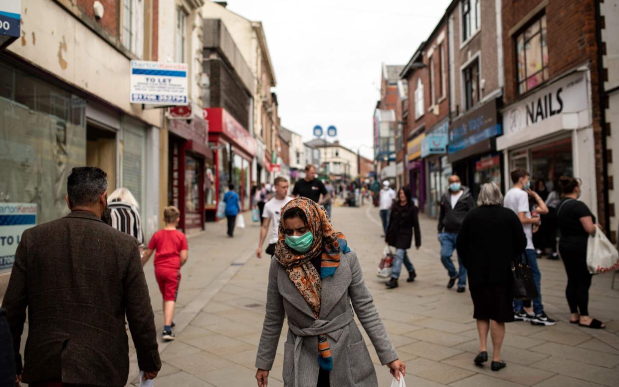 Pedestrians wear face masks as they walk down a street in Oldham, where virus cases are rising - Oli Scarff/AFP