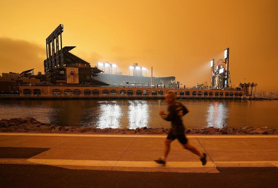 A jogger runs past a professional baseball park under eerily orange skies.