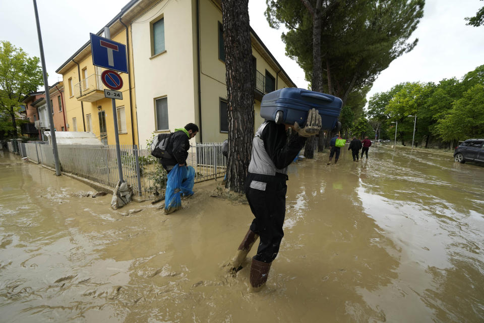 A man carries a suitcase in a flooded road in Faenza, Italy, Thursday, May 18, 2023. Exceptional rains Wednesday in a drought-struck region of northern Italy swelled rivers over their banks, killing at least eight people, forcing the evacuation of thousands and prompting officials to warn that Italy needs a national plan to combat climate change-induced flooding. (AP Photo/Luca Bruno)