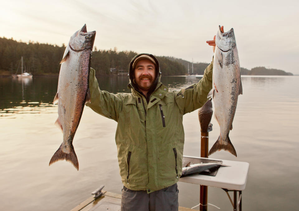 A guy holding up two large fish he caught