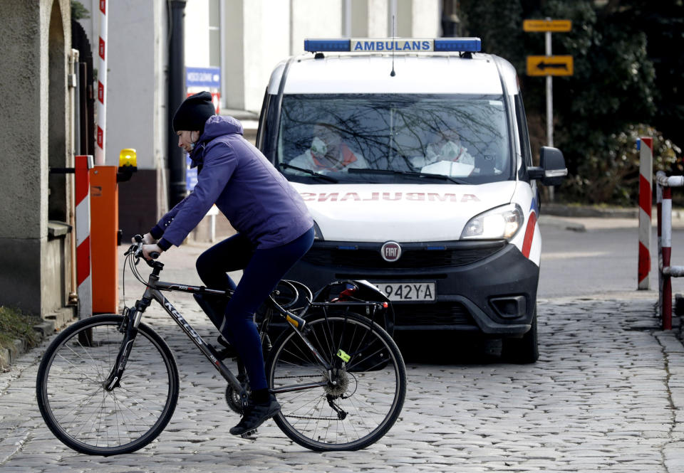 A cyclist passes in front of an ambulance by an infectious diseases hospital in Warsaw, Poland, on Thursday, March 25, 2021. Amid a sharp spike in new infections and hospitalizations that are bringing the health care to its limits, Poland has stepped up pandemic measures for two weeks starting Saturday, including fewer people to be allowed into churches at the holiday time. (AP Photo/Czarek Sokolowski)