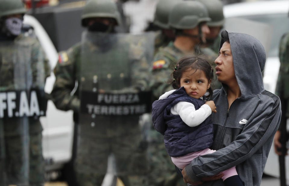 Un hombre que carga a una niña sale de un camino después de que soldados llegaran a reabrirlo en Quito, Ecuador, el lunes 7 de octubre de 2019. (AP Foto/Dolores Ochoa)