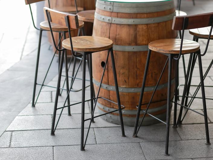 a barrel table with several brown stool chairs surrounding it all on outdoor, gray tile