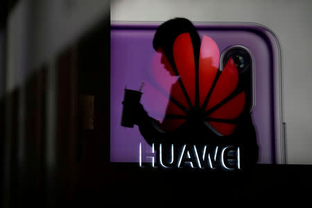 FILE PHOTO - A man walking past a Huawei P20 smartphone advertisement is reflected in a glass door in front of a Huawei logo at a shopping mall in Shanghai, China December 6, 2018. REUTERS/Aly Song/File Photo