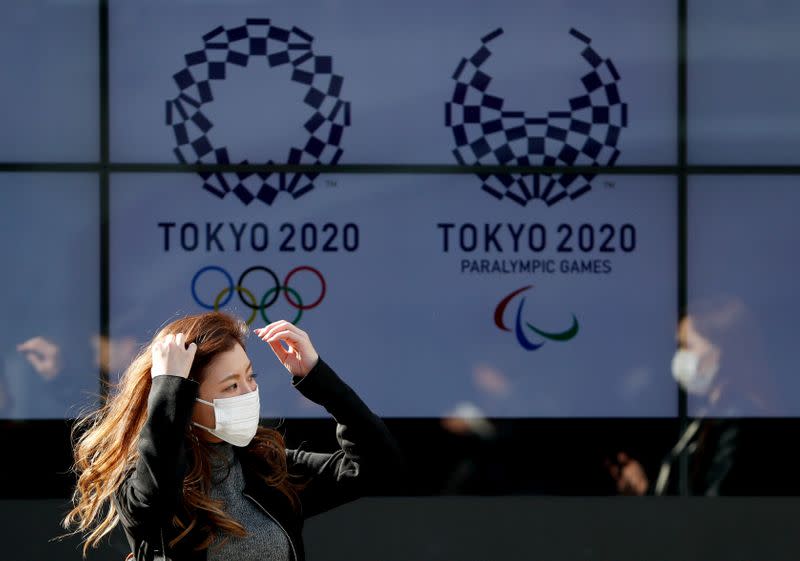 A passerby wearing a protective face mask following an outbreak of the coronavirus disease (COVID-19) walks past a screen displaying logos of Tokyo 2020 Olympic and Paralympic Games in Tokyo