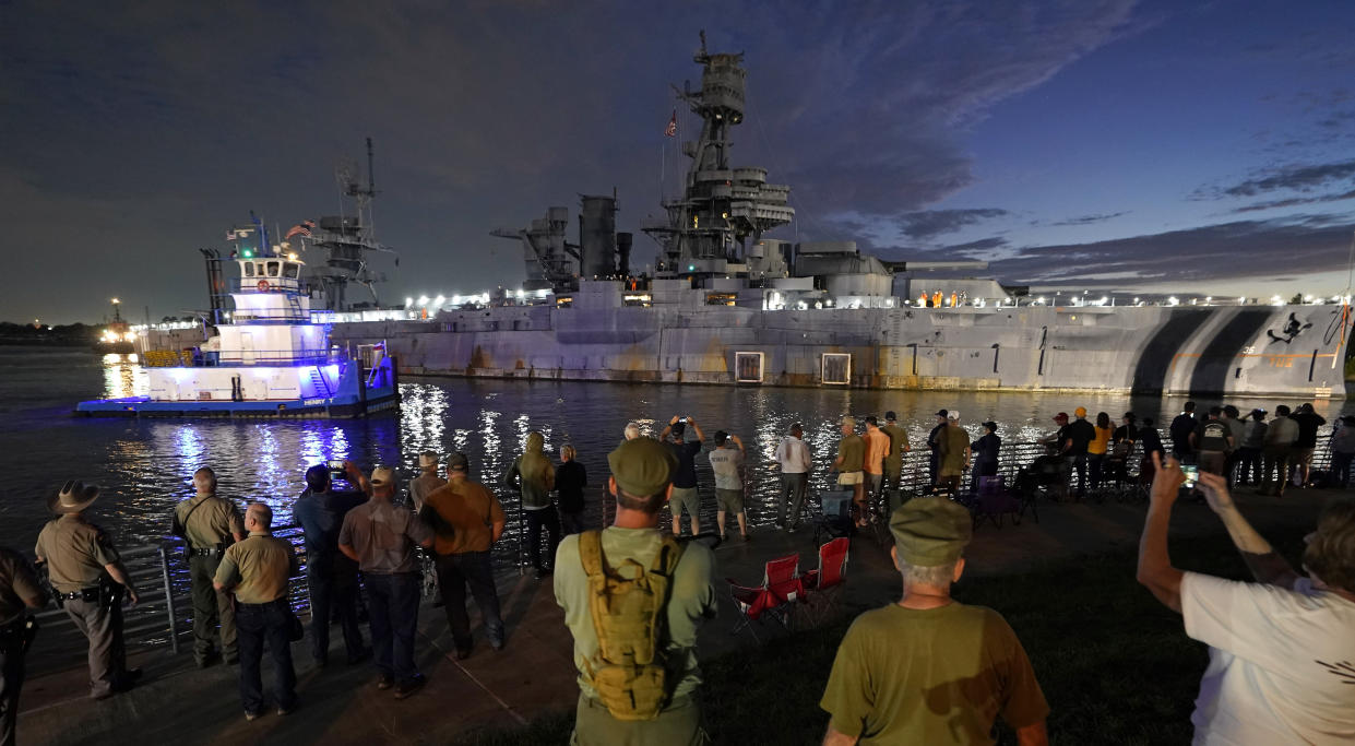 People watch as the USS Texas is moved from the dock Wednesday, Aug. 31, 2022, in La Porte, Texas. The vessel, which was commissioned in 1914 and served in both World War I and World War II, is being towed down the Houston Ship Channel to a dry dock in Galveston where it will undergo an extensive $35 million repair. (AP Photo/David J. Phillip)