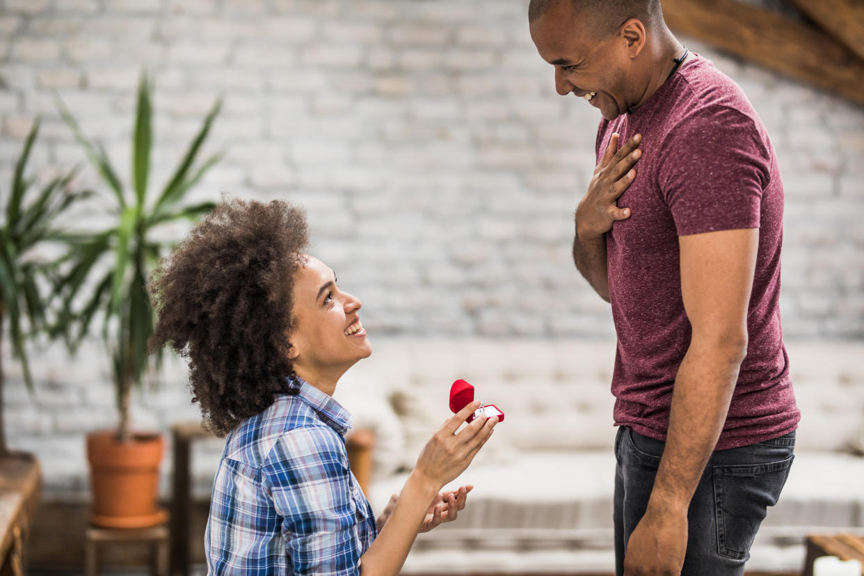 Happy black woman proposing to her boyfriend in the living room. leap year