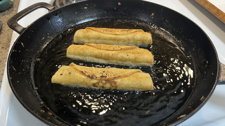 three taquitos frying in skillet