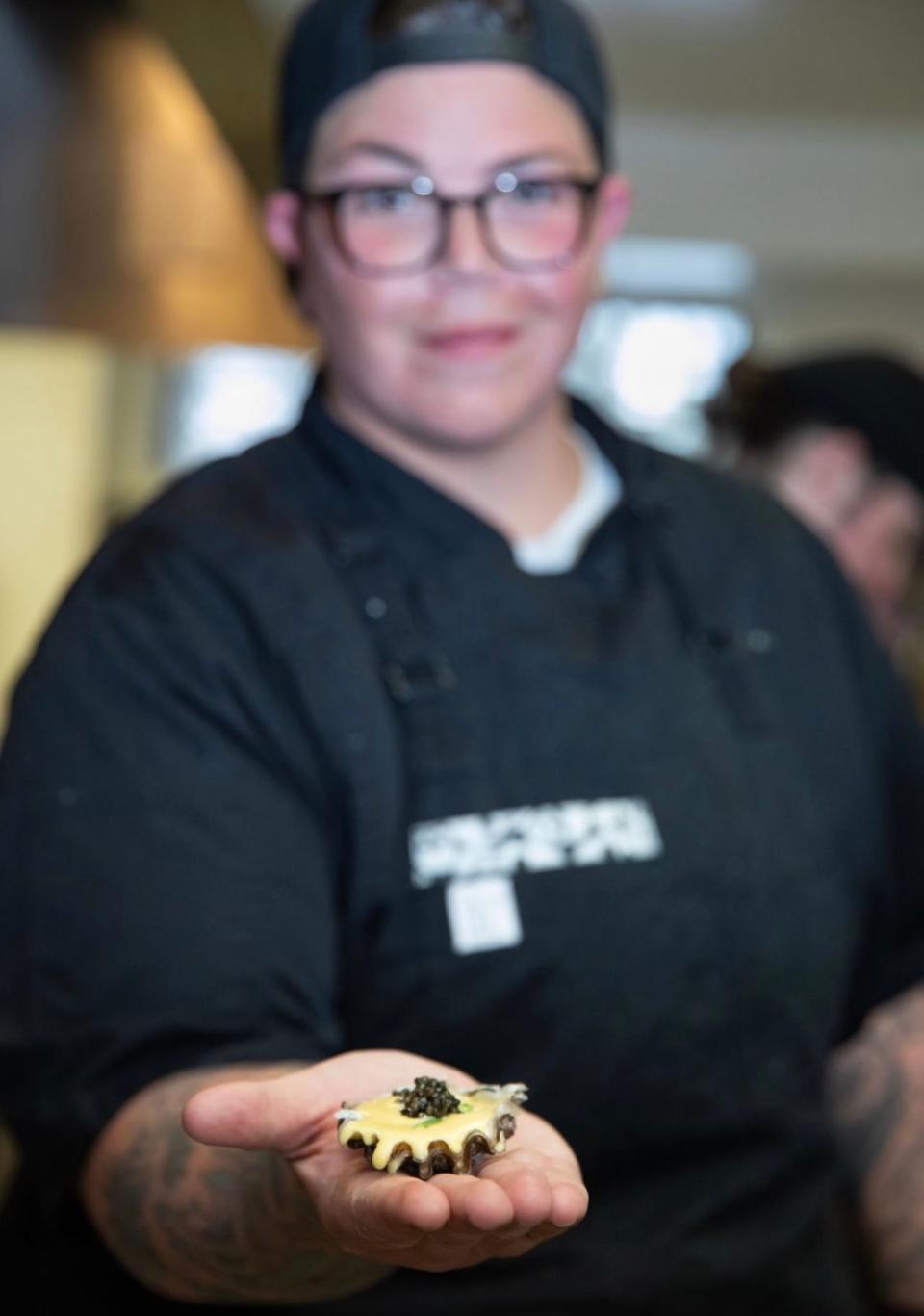 Food Network's Chef Britt Rescigno holding a shucked Totten Inlet Oyster with champagne brown butter sabayon, and topped with sea beans and sterling caviar.