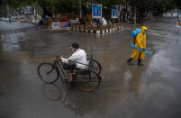 A man rides on a tricycle past a civic worker sanitizing a deserted road during a fresh lockdown imposed in Gauhati, Assam state, India, Sunday, July 12, 2020. India is the world’s third worst-affected country by the coronavirus. (AP Photo/Anupam Nath)