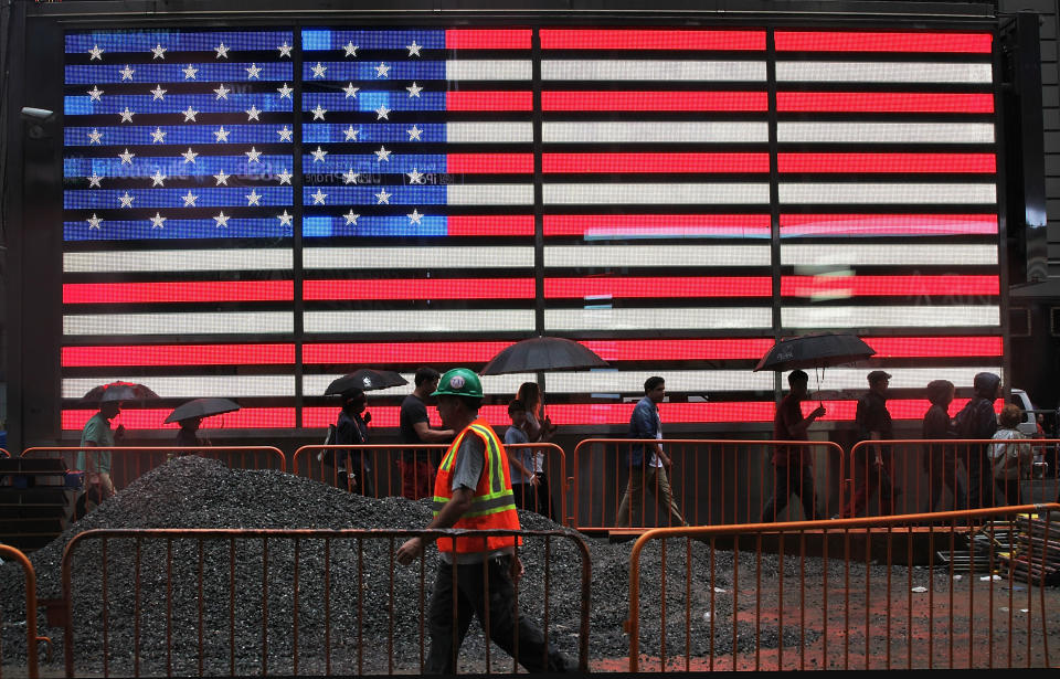 NUEVA YORK, NUEVA YORK - 22 DE AGOSTO: Un peatón y un trabajador de la construcción pasan junto a una bandera estadounidense encendida bajo la lluvia en Times Square el 22 de agosto de 2013 en la ciudad de Nueva York.  Se espera que la lluvia caída esta tarde en la ciudad desaparezca mañana.  (Foto: Mario Tama/Getty Images)