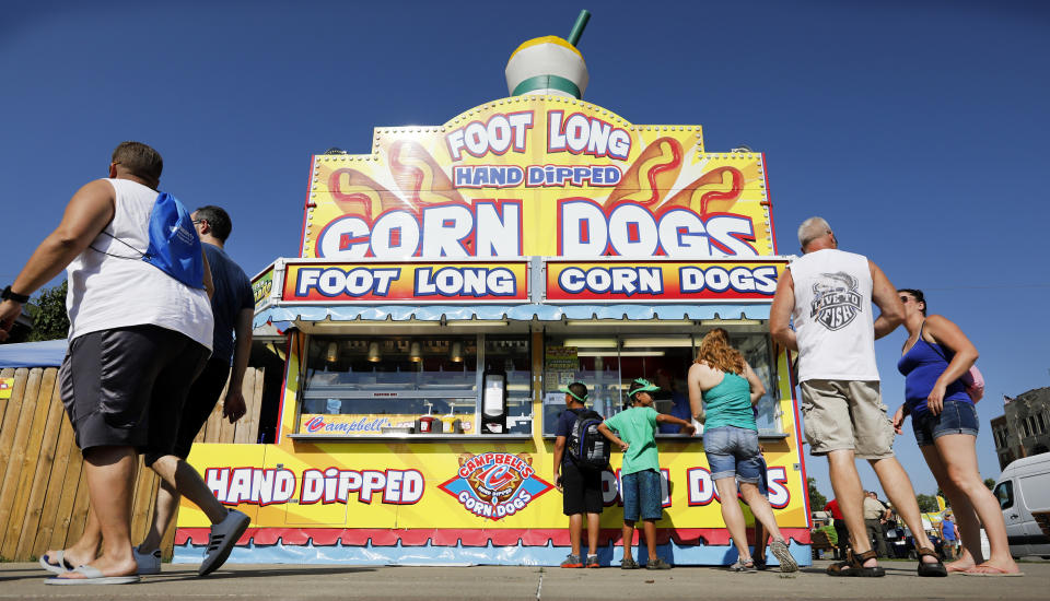 FILE - In this Aug. 9, 2018 file photo, Iowa State fairgoers line up to get a corn dog at a concession stand during the opening day of the Iowa State Fair in Des Moines, Iowa. With coronavirus cases rising throughout Iowa and around the nation, health experts are becoming increasingly worried about next month's Iowa State Fair, which will bring more than 1 million people to Des Moines. (AP Photo/Charlie Neibergall, File)