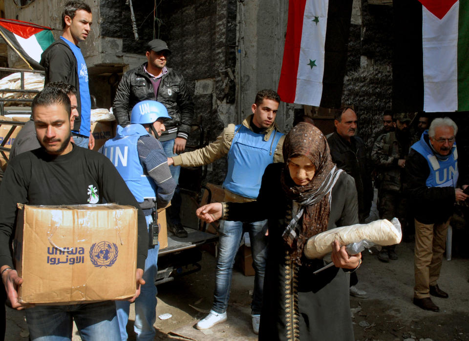 In this photo released by the Syrian official news agency SANA, Palestinian residents of the besieged refugee camp of Yarmouk carry supplies given to them by the United Nations at the gate of the camp on the southern edge of the Syrian capital Damascus, Syria, Thursday, Jan. 30, 2014. The U.N. says 600 food parcels were distributed in the camp where activists say at least 85 people have died as a result of lack of food and medicine since mid-2013. (AP Photo/SANA)