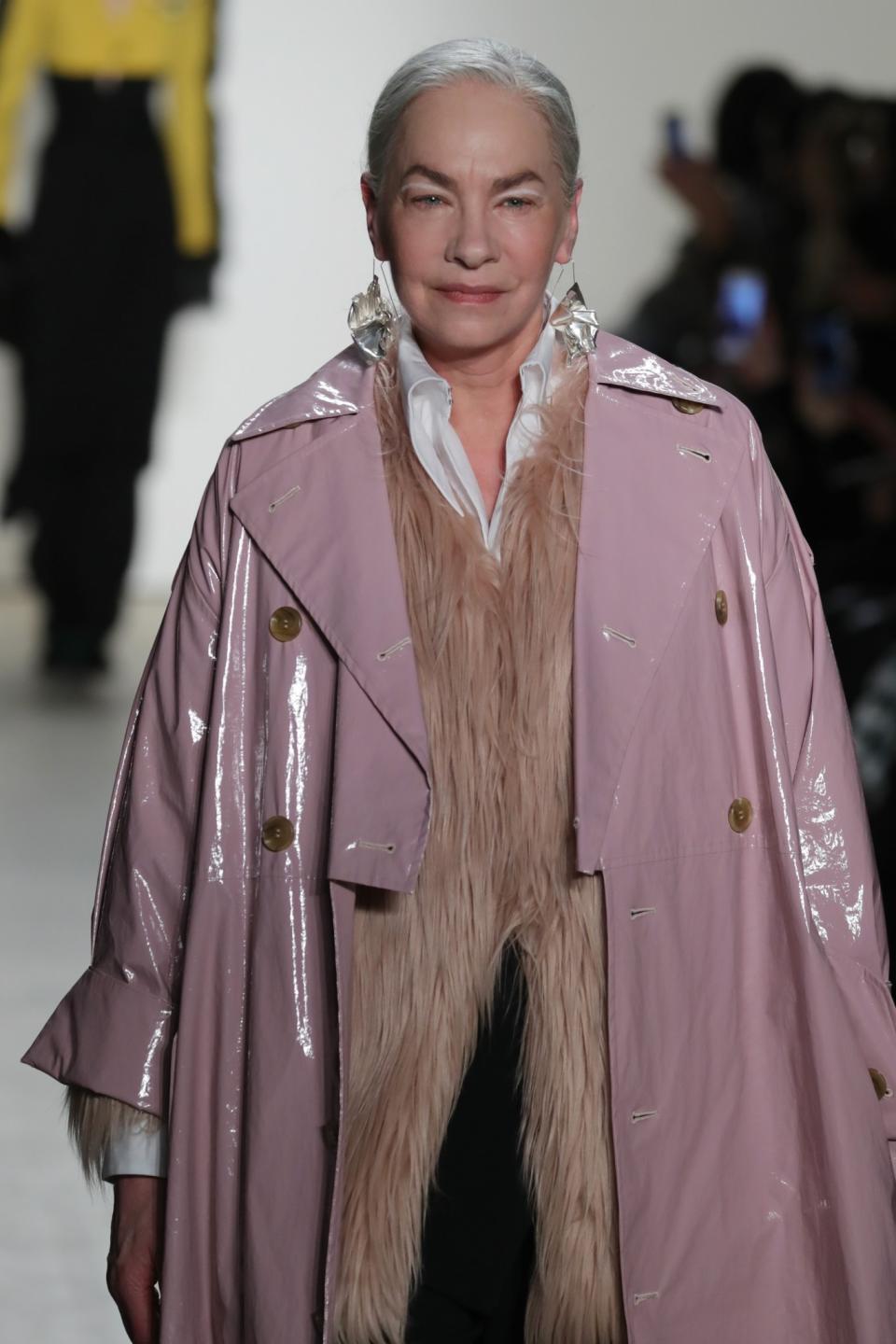 A stunning older female model walks the Tome show wearing a pastel pink vinyl coat and matching fur jacket.