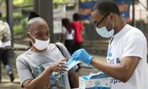 FILE - In this July 8, 2020, file photo, Stephane Labossiere, right, with the Mayor's Office of Immigrant Affairs, hands out masks and printed information about free COVID-19 testing in Brooklyn being offered by NYC Health + Hospitals, in New York. As coronavirus rages out of control in other parts of the U.S., New York is offering an example after taming the nation’s deadliest outbreak this spring — but also trying to prepare in case another surge comes. (AP Photo/Mark Lennihan, File)